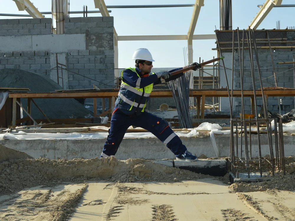 Bauarbeiter mit Helm und Warnweste neben Bewehrungsstahl