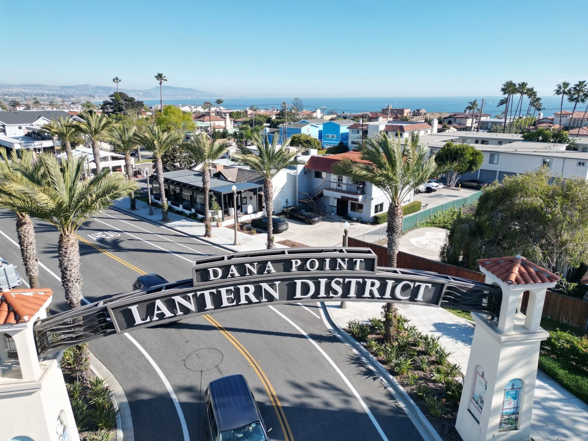 The Dana Point Lantern District entry arch with palm-lined streets and the ocean beyond
