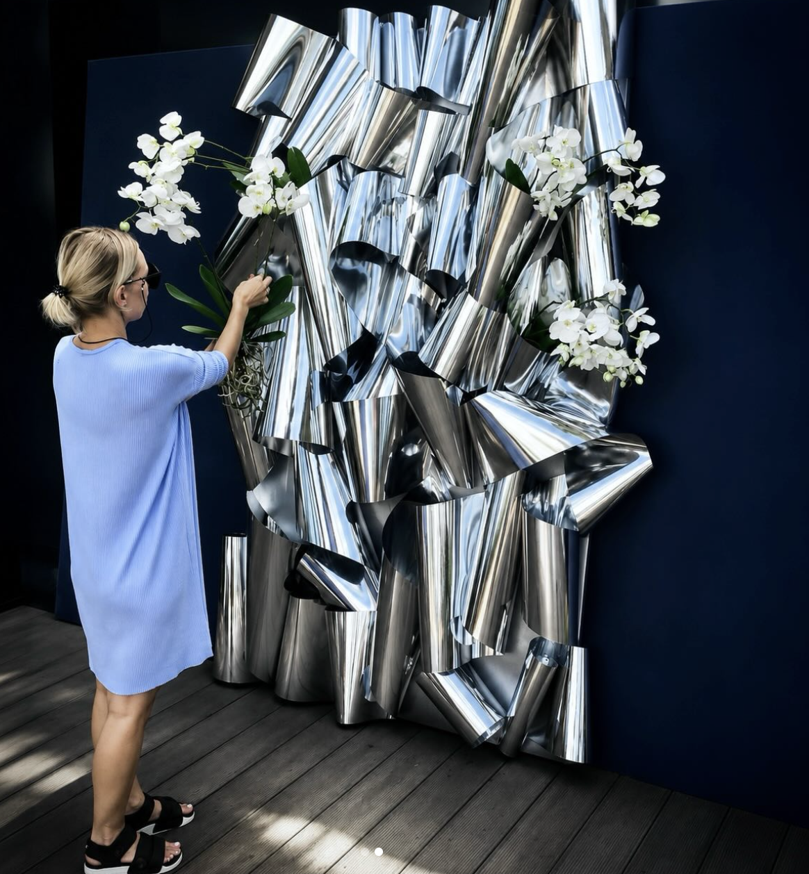 Yuliia Hyatt placing white phalaenopsis orchids into a large mirrored installation during an on-site setup