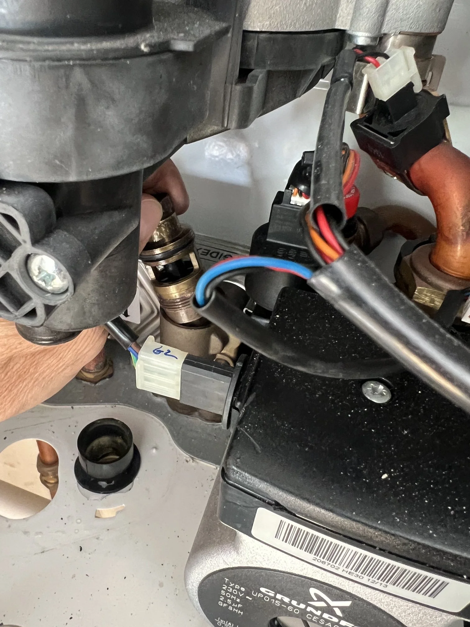 Engineer removing an internal valve component from a combi boiler for inspection, with the circulating pump visible below