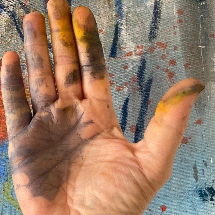 Marcus Bacher's paint-stained hand held against one of his abstract canvases.