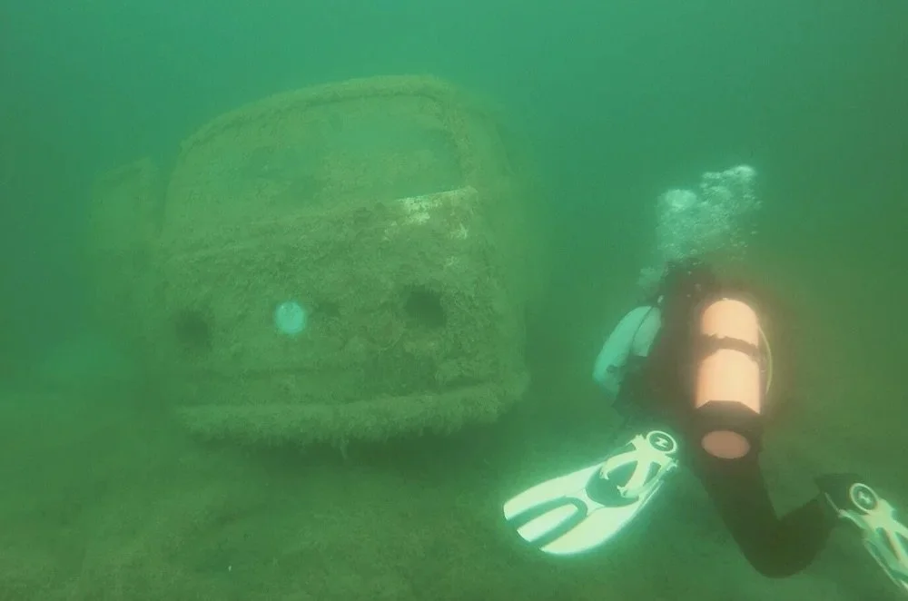 The sunken Volkswagen bus at Sand Hollow, front on and heavily silted, with the VW badge still visible and a diver finning past on the right