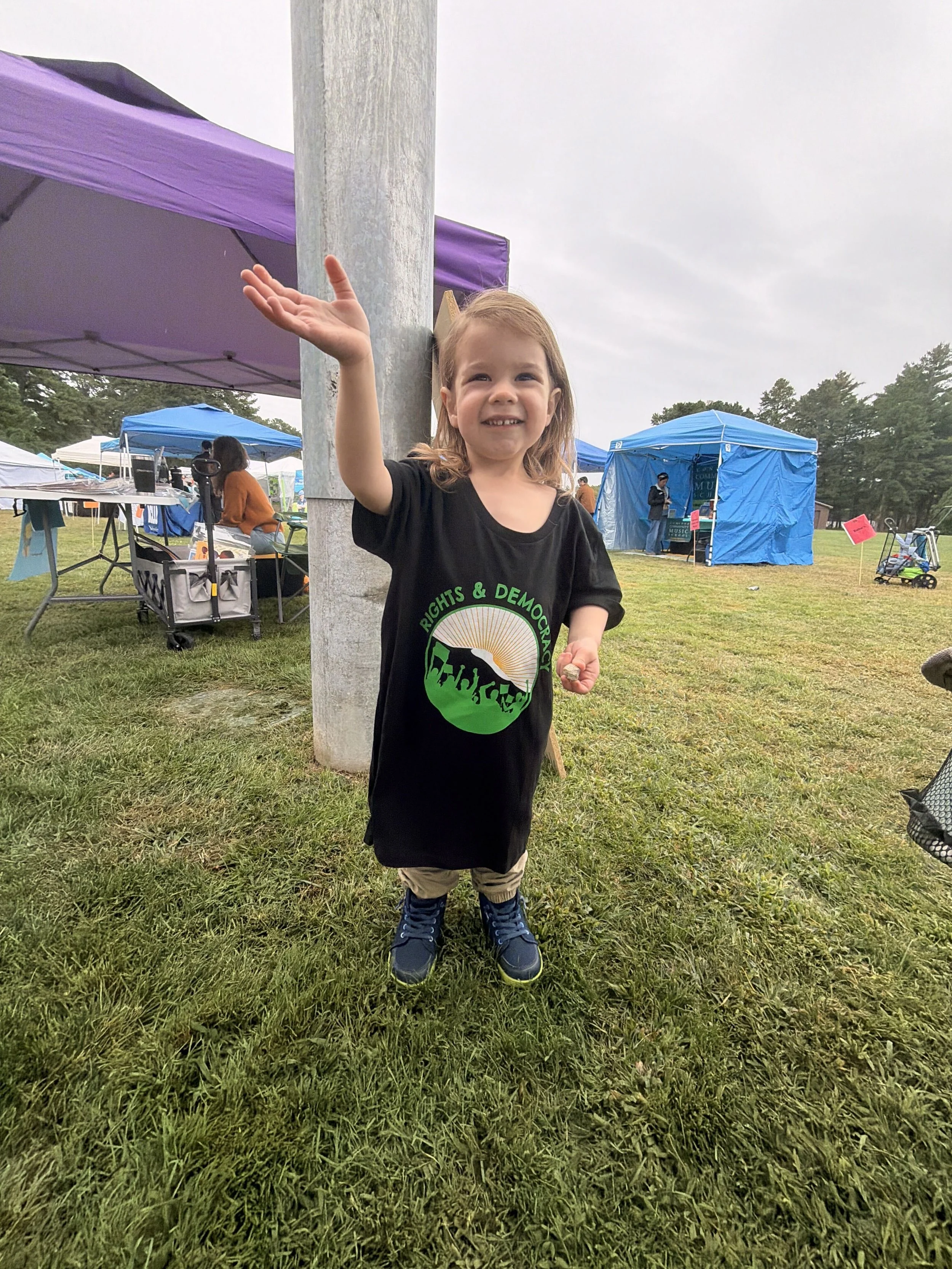 A smiling child wearing a Rights and Democracy shirt at an outdoor event.