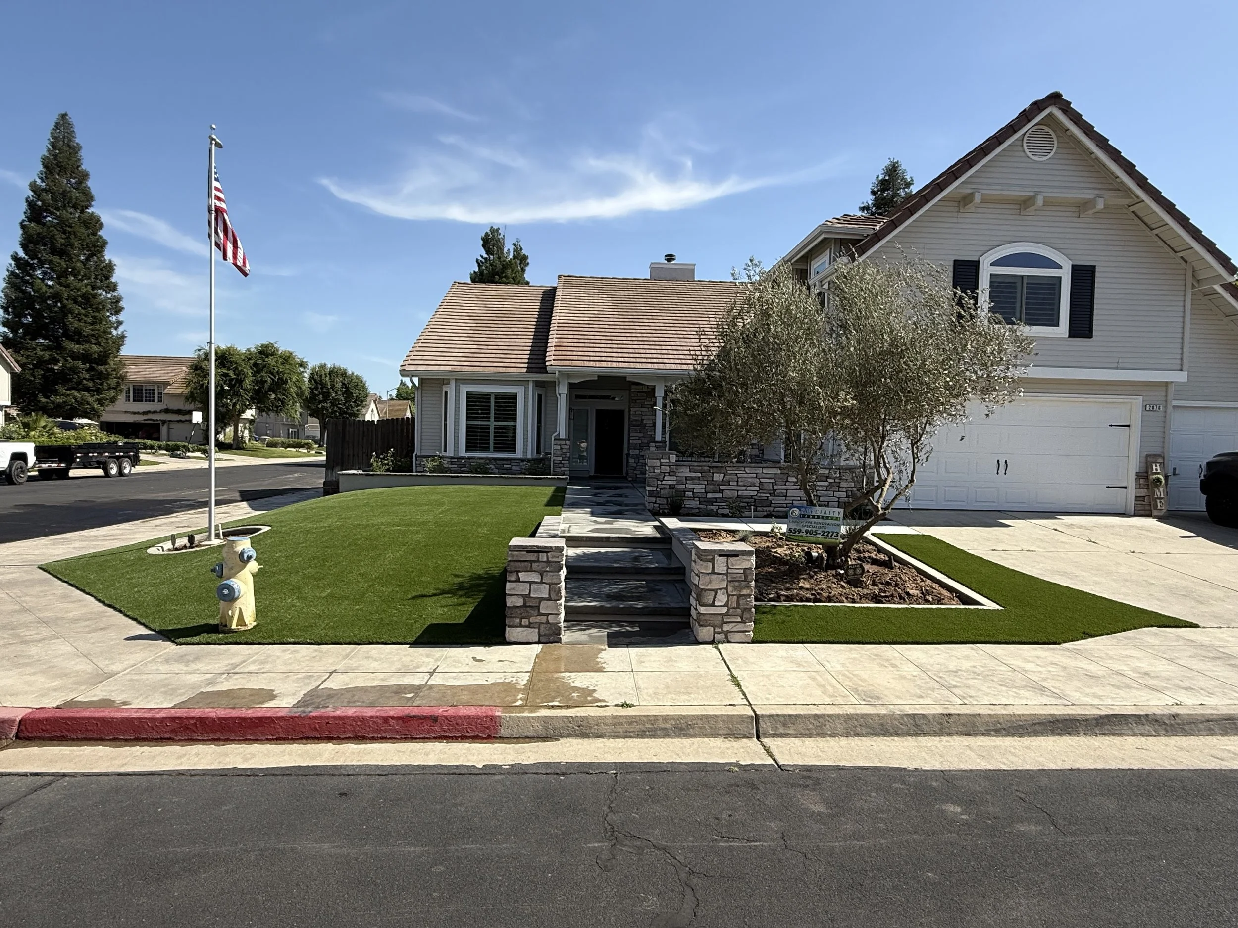 Front yard with a mown lawn, flagpole and mulch beds at a Fresno-area home