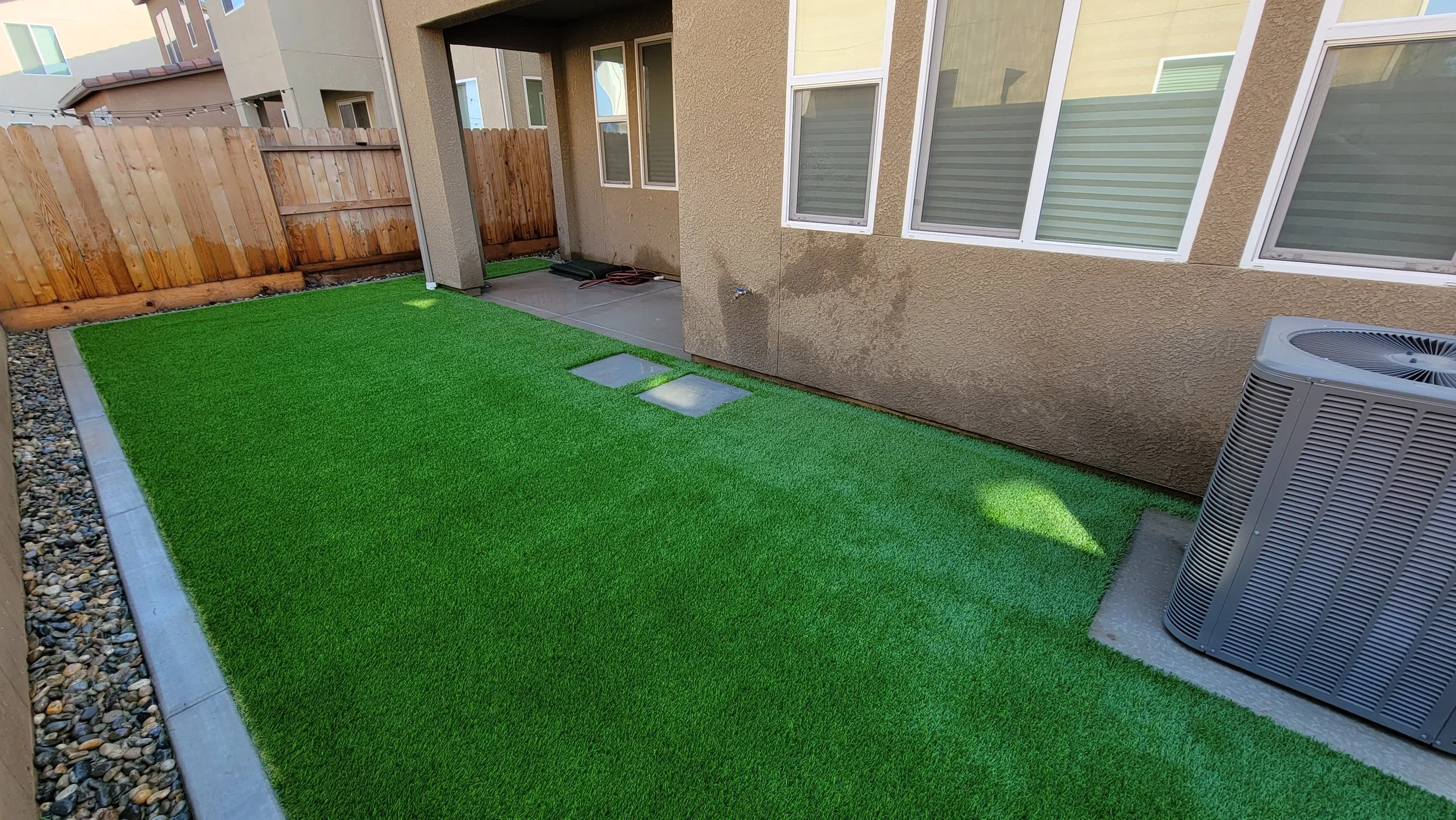 Backyard artificial turf with concrete stepping pads and a wood fence