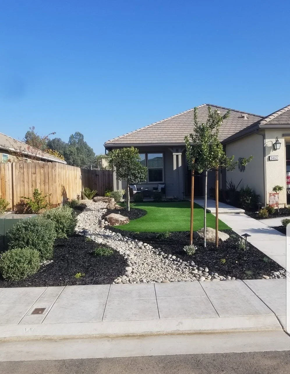 Finished front yard with artificial turf, boulders, young trees and mulch beds
