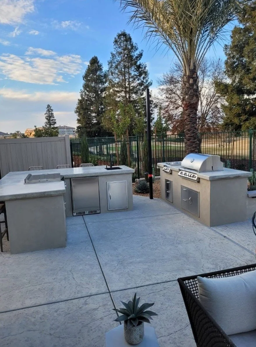 Outdoor kitchen island with built-in grills beside an artificial turf lawn by Specialty Landscape