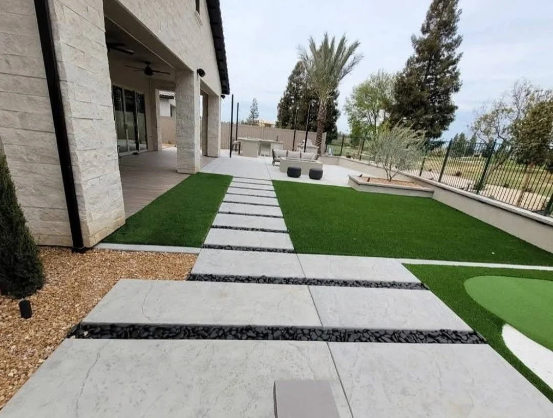 Modern backyard designed and built by Specialty Landscape with paver walkway, artificial turf and planted borders