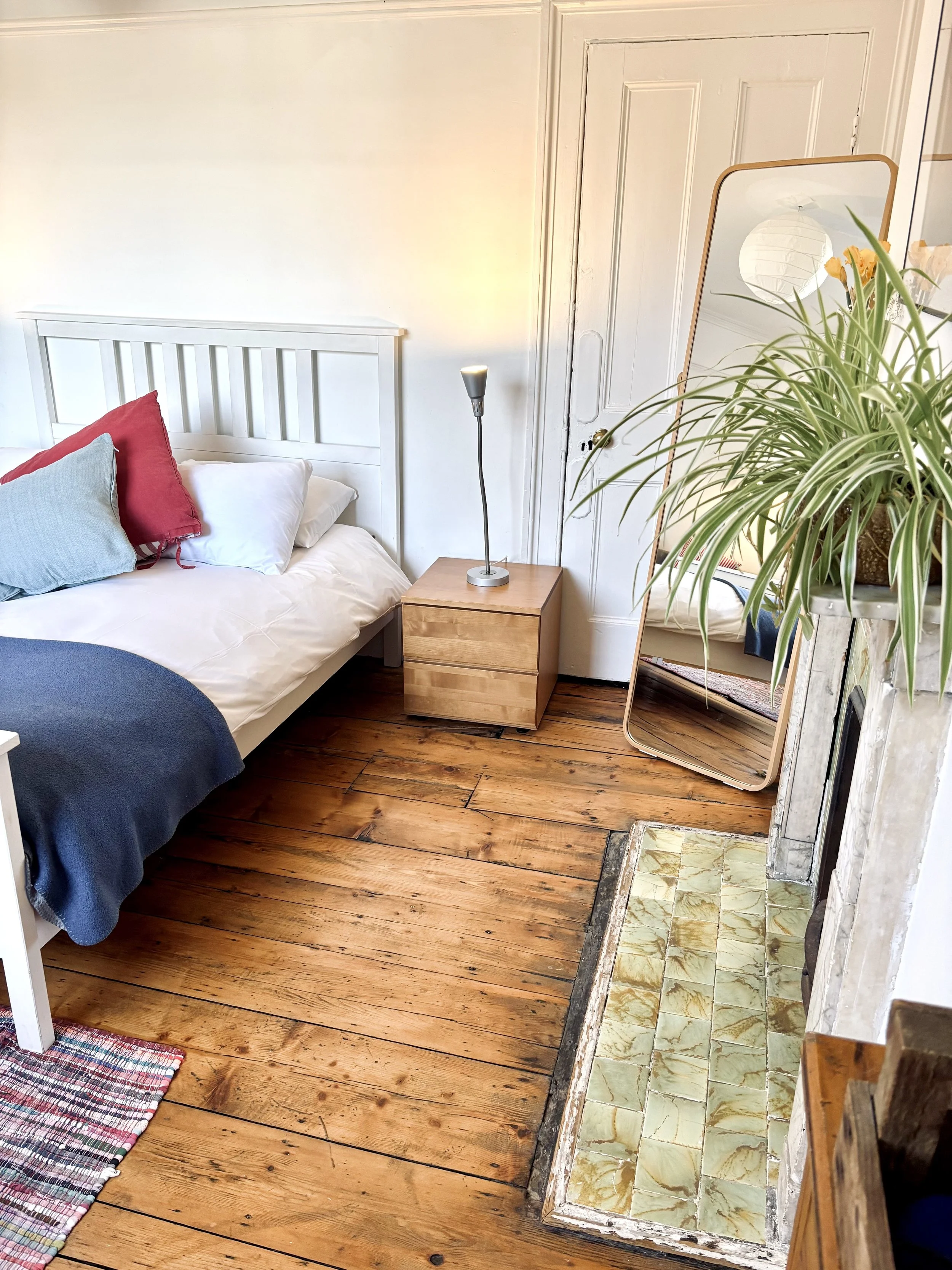 Room 3 garden-facing double bedroom with navy throw, mirror, indoor plant and original green-tiled fireplace at Central Victorian House in Camden Town