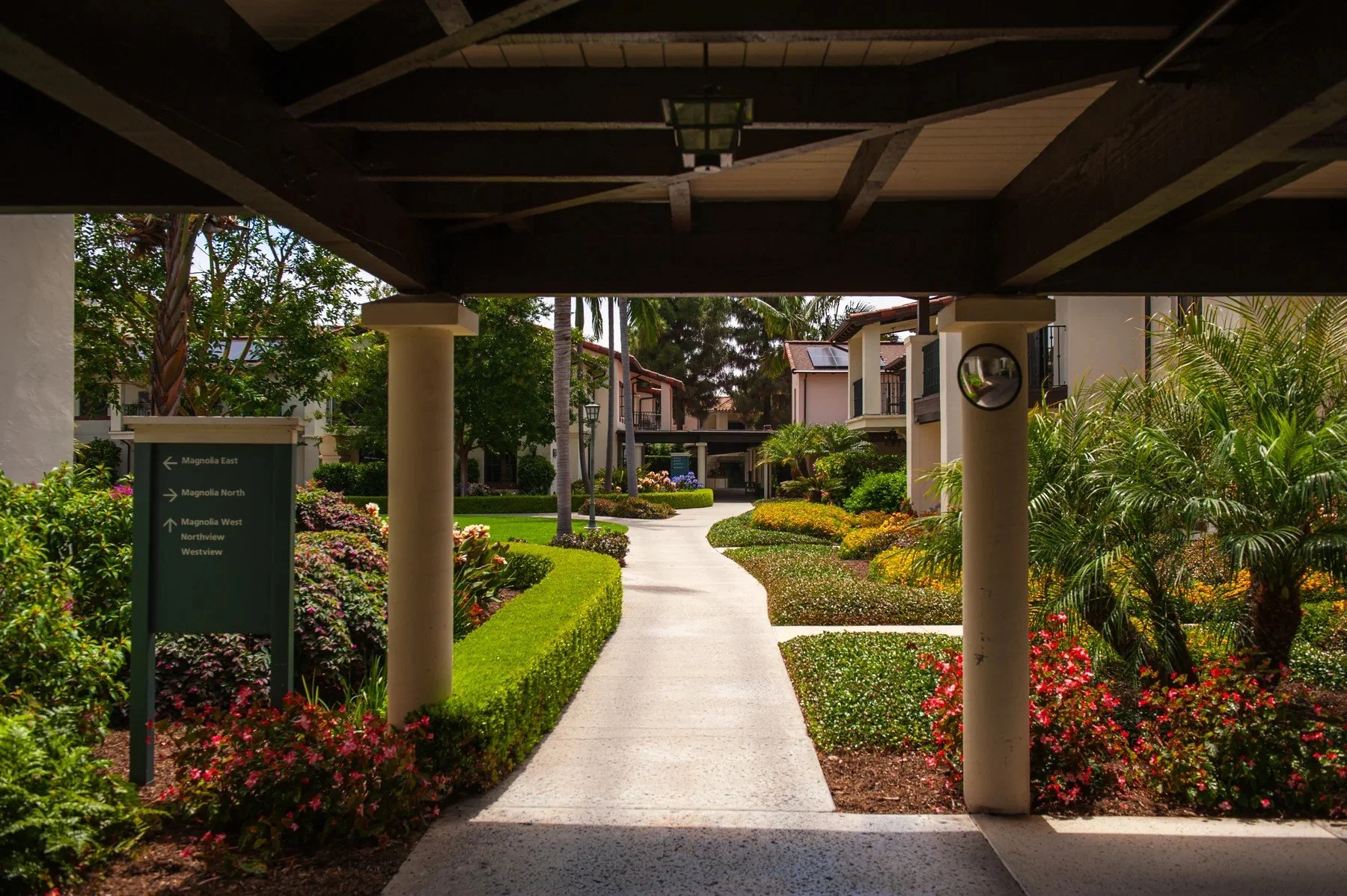 A covered walkway opening onto clipped hedges, flowers, and palms at Samarkand