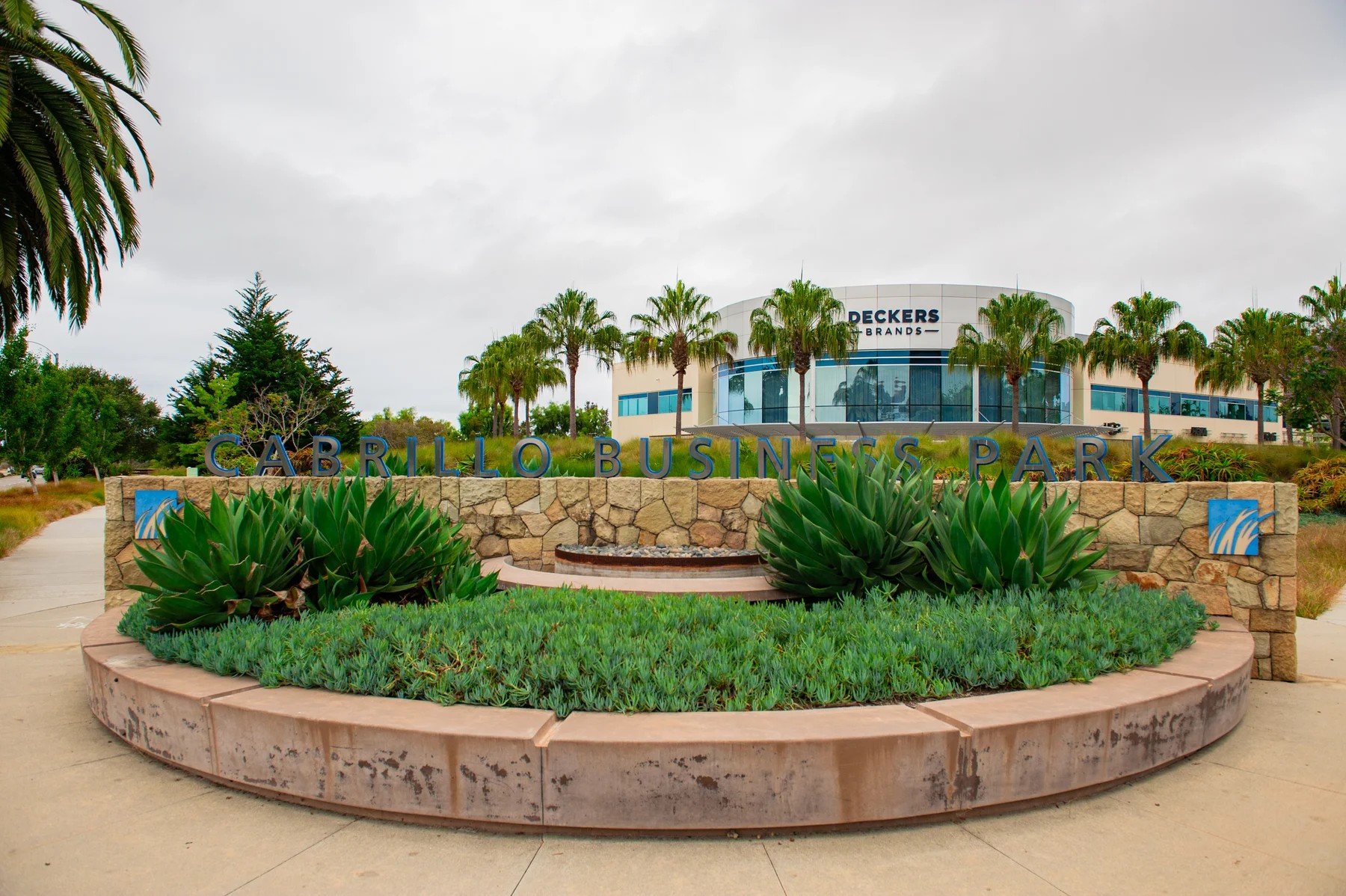 The Cabrillo Business Park monument sign behind a curved succulent planter, with Deckers beyond