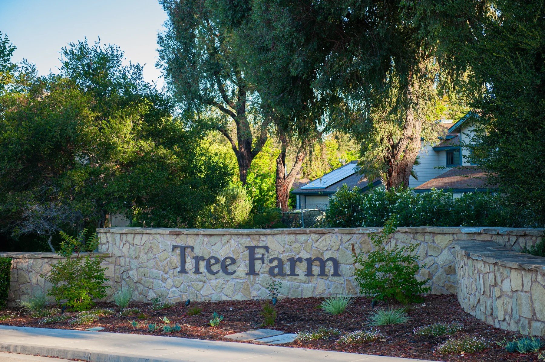 Tree Farm name on a stone entrance wall framed by mature trees and garden planting