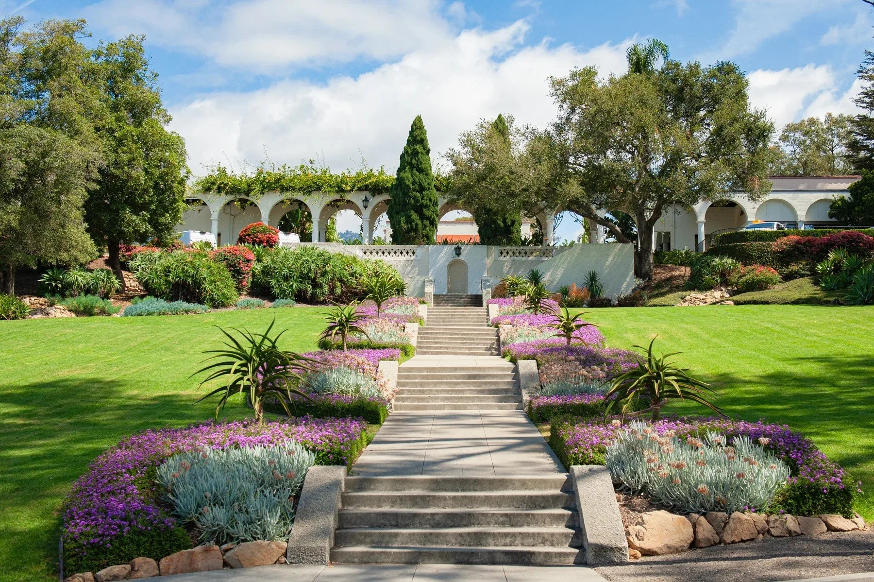 Head-on view of the central staircase, colorful flower beds, and white arches at Riviera Park