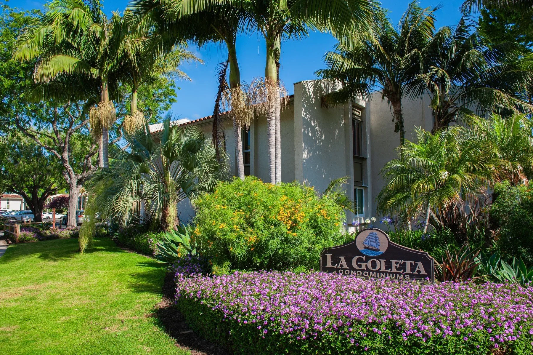 La Goleta Condominiums monument sign surrounded by palms and pink flowers