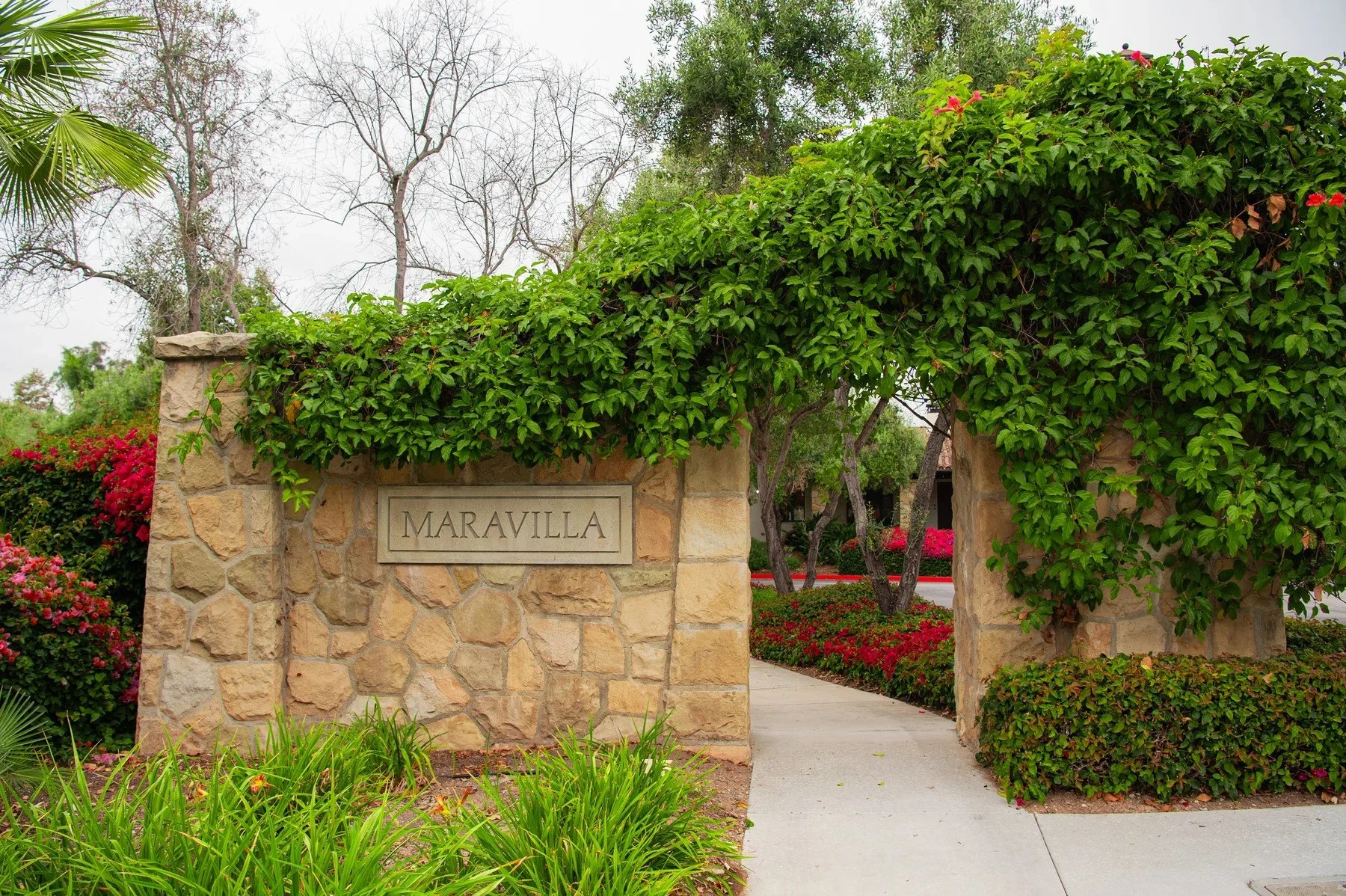 Maravilla monument sign in a stone gateway framed by climbing greenery and flowers