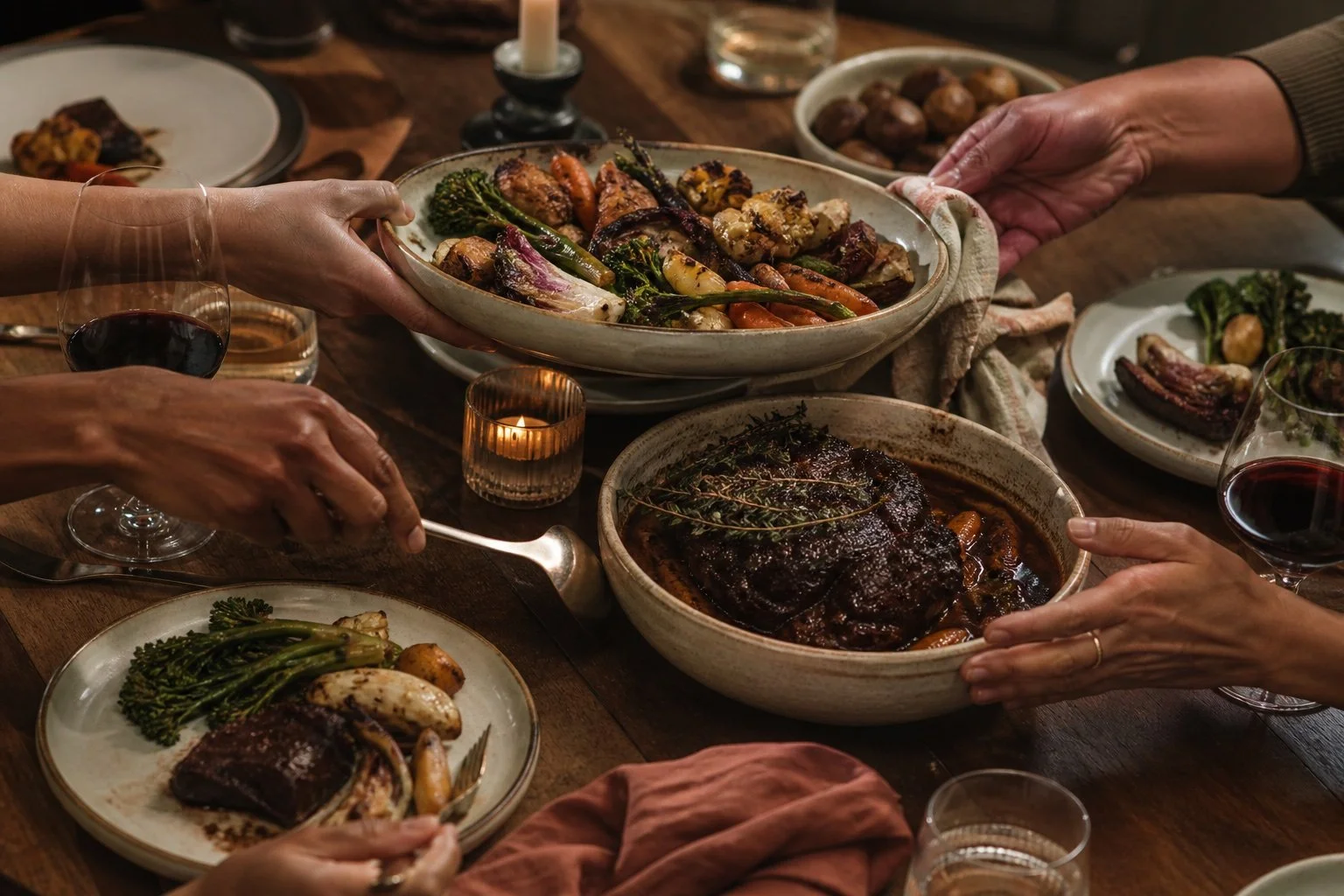 Hands passing shared platters around a warmly lit dinner table