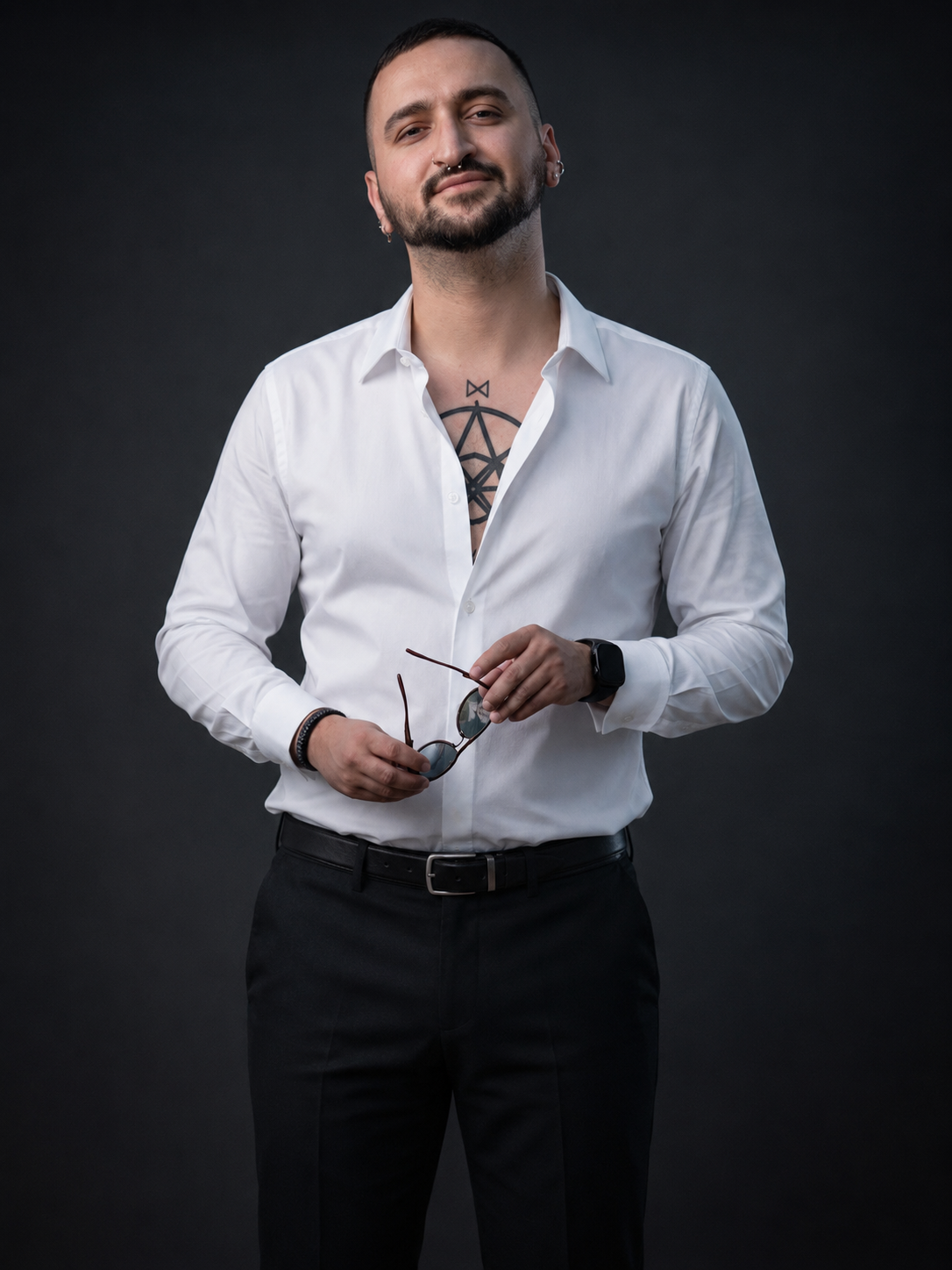 Denis in white shirt and dark trousers holding sunglasses