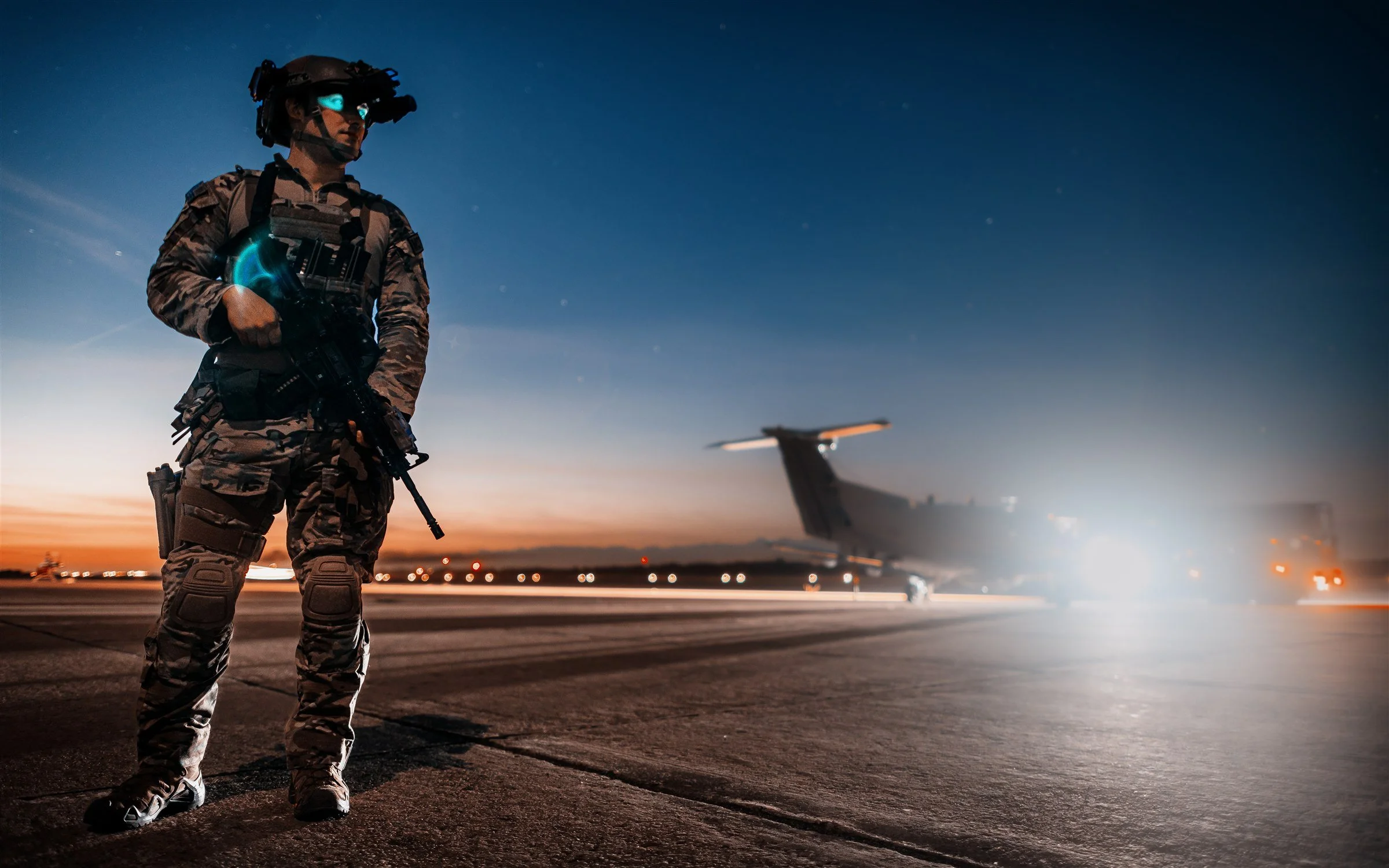 Special operations communications specialist on the flightline at twilight, instrument glow on chest, U-28A Draco in distance
