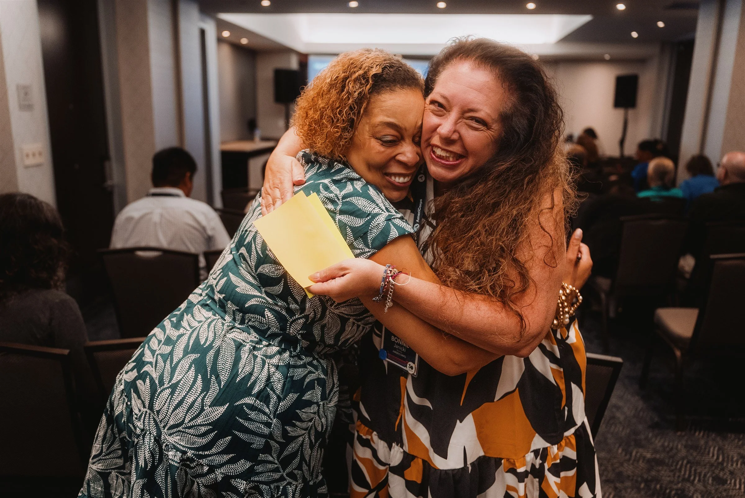 Two attendees mid-laugh in candid embrace at an event