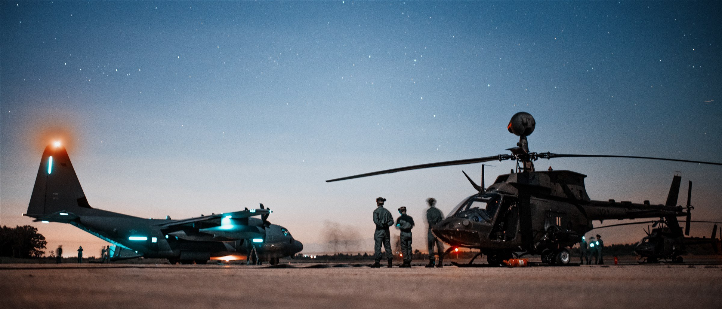 C-130 and helicopter at a forward-area refueling point under a starry twilight sky, crew in silhouette between aircraft
