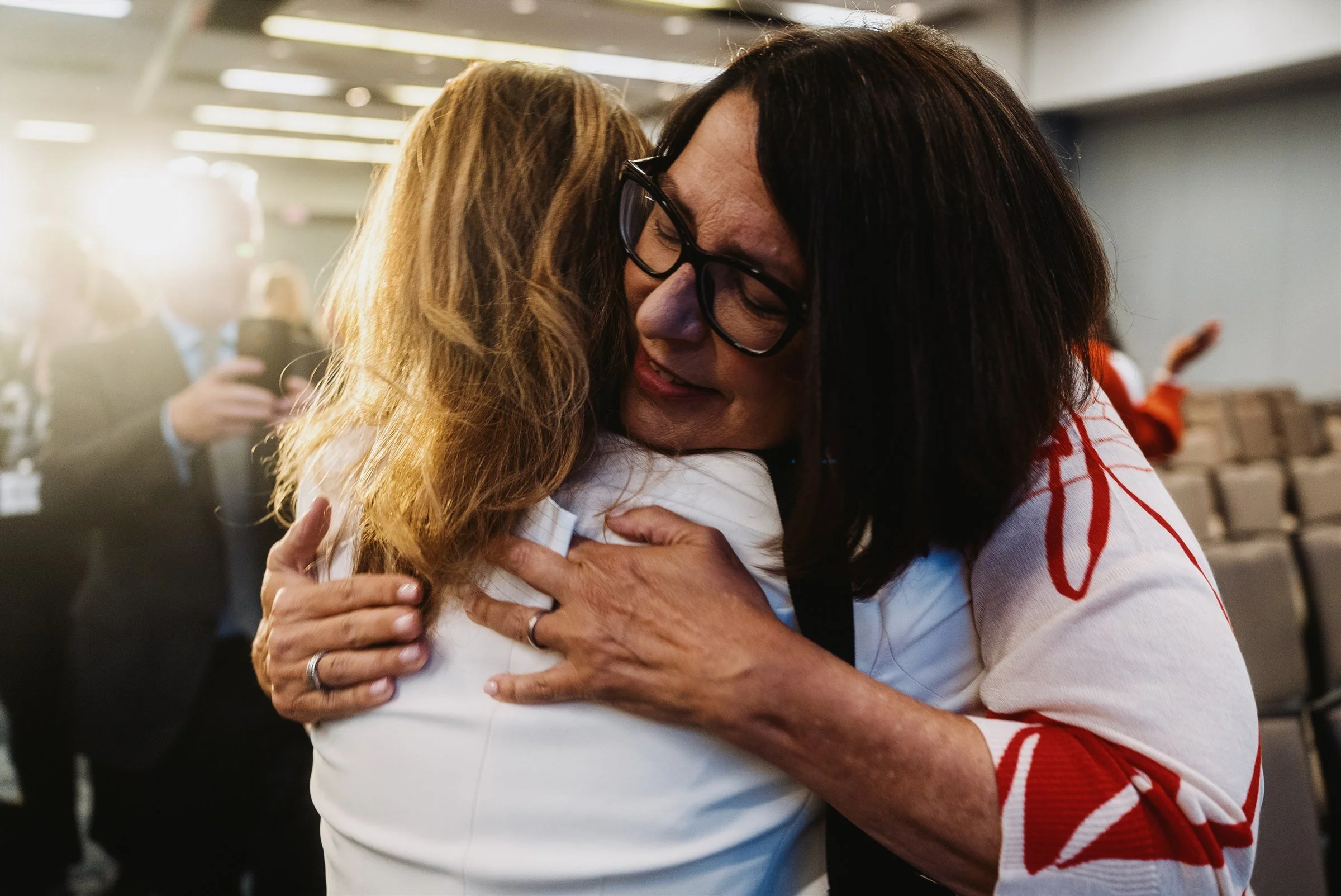 Two women in tight emotional embrace, backlit by warm afternoon sun