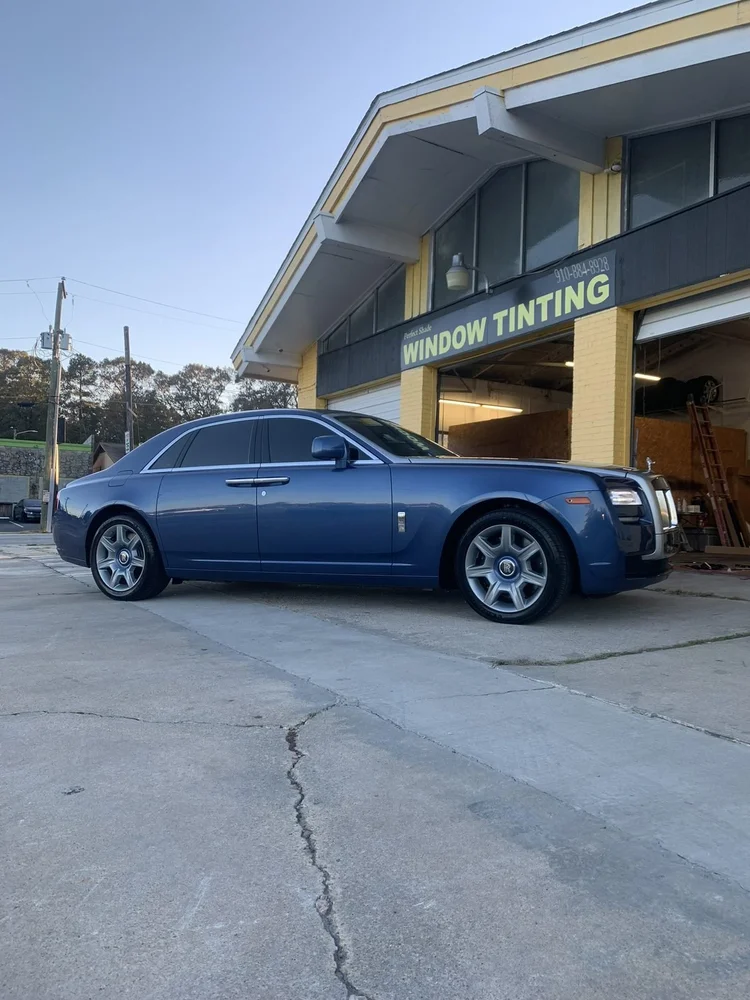 Two-tone blue and black Rolls-Royce Ghost with tinted windows in front of Perfect Shade