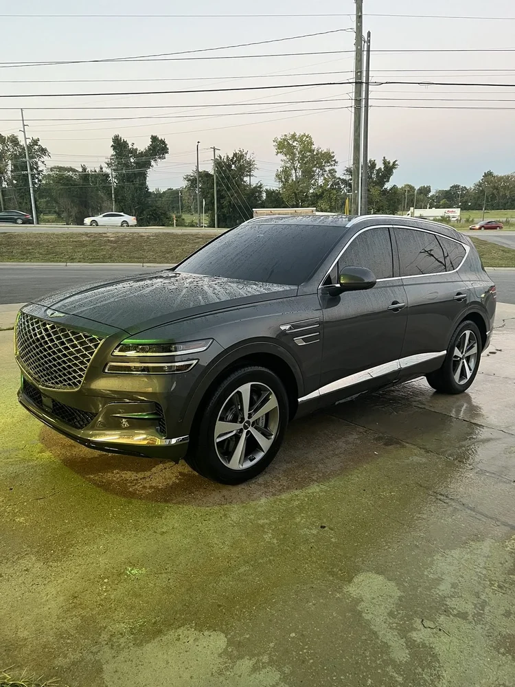 Dark Genesis SUV with tinted windows on a wet lot outside the shop