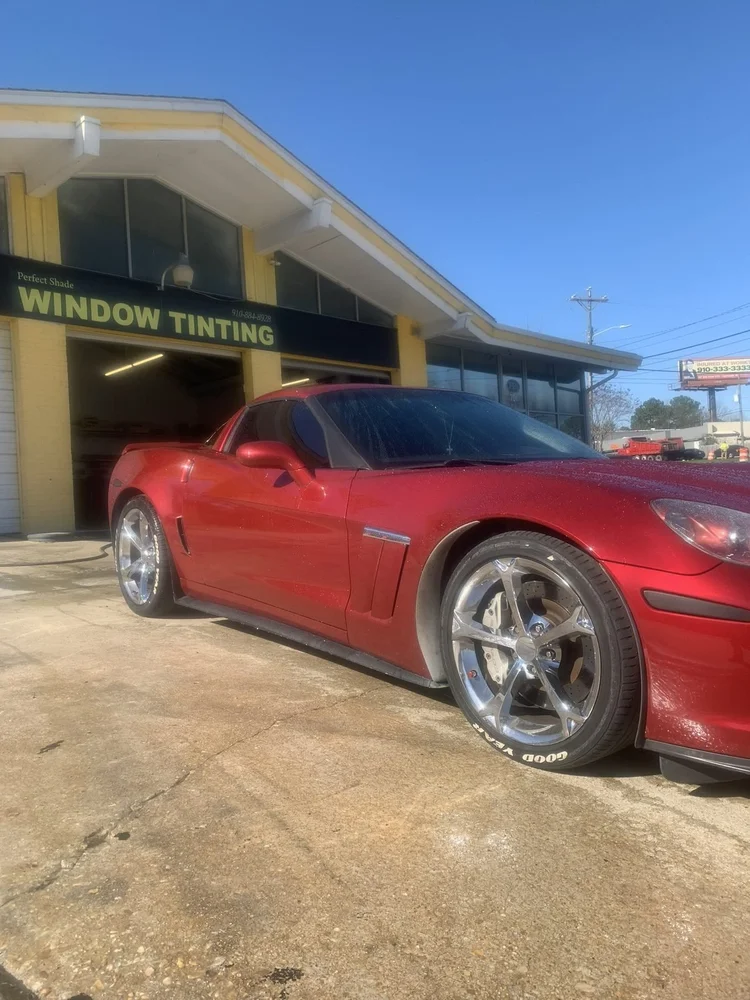 Red Chevrolet Corvette with tinted windows in front of the Window Tinting sign