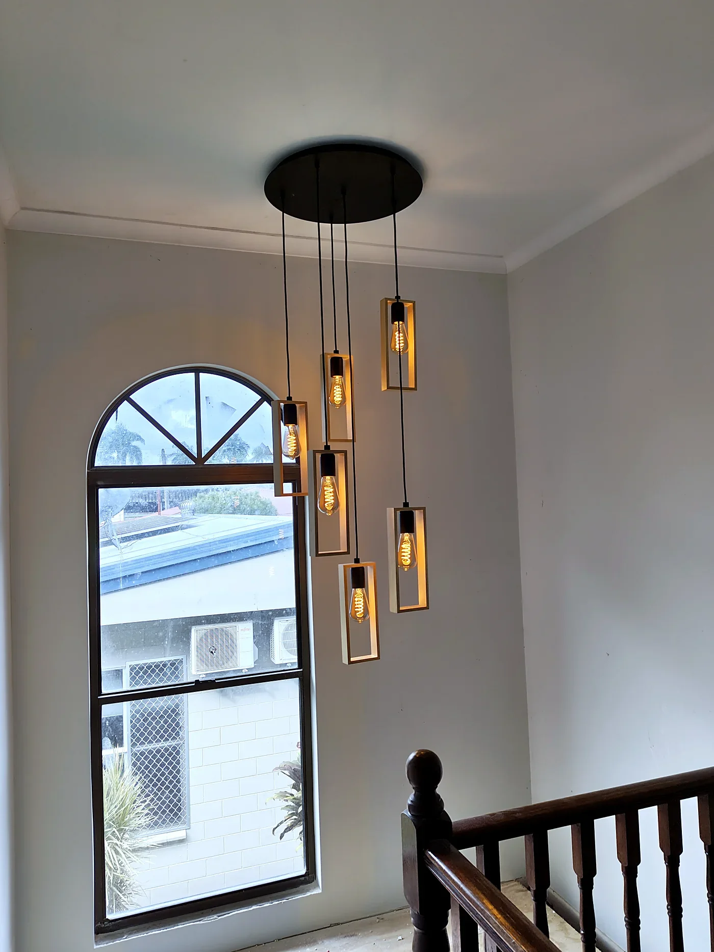 A multi-drop feature pendant light hanging in a stairwell beside an arched window