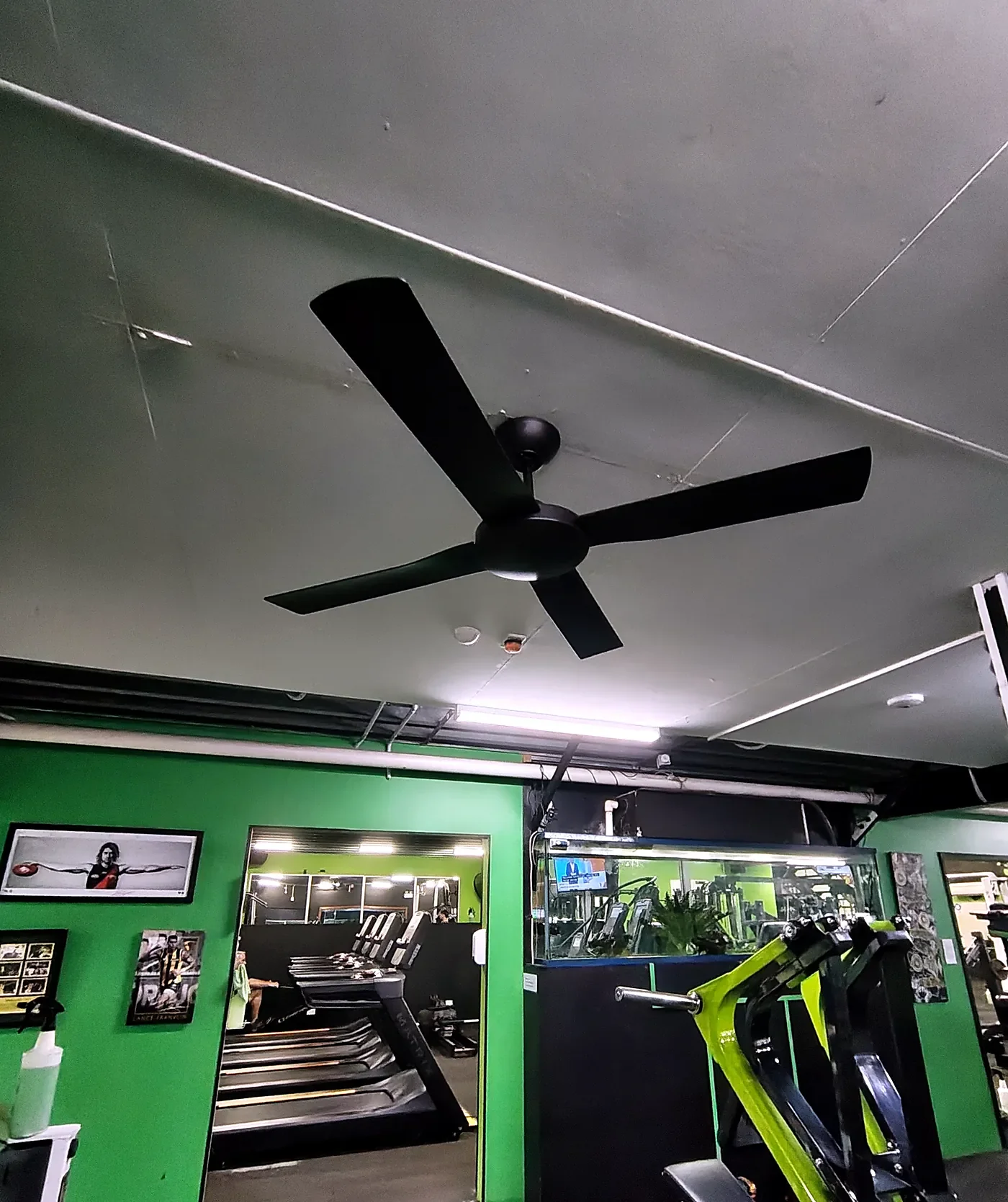 After: a new black four-blade ceiling fan on a grey ceiling in a green gym