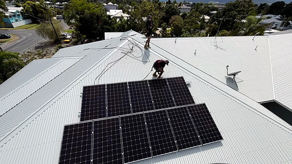 Two workers in safety harnesses lifting solar panels back onto a Cairns roof