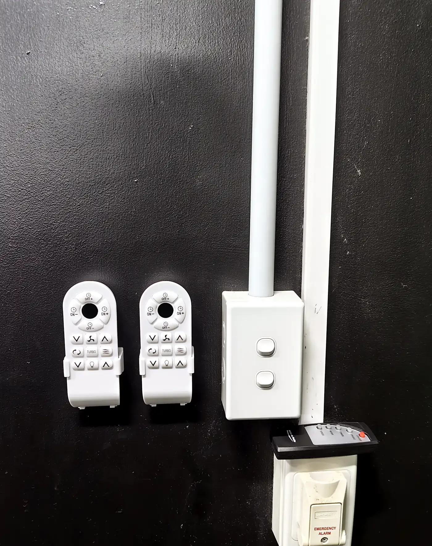 Newly installed wall-mounted fan remote holders beside a two-gang switch on a black gym wall