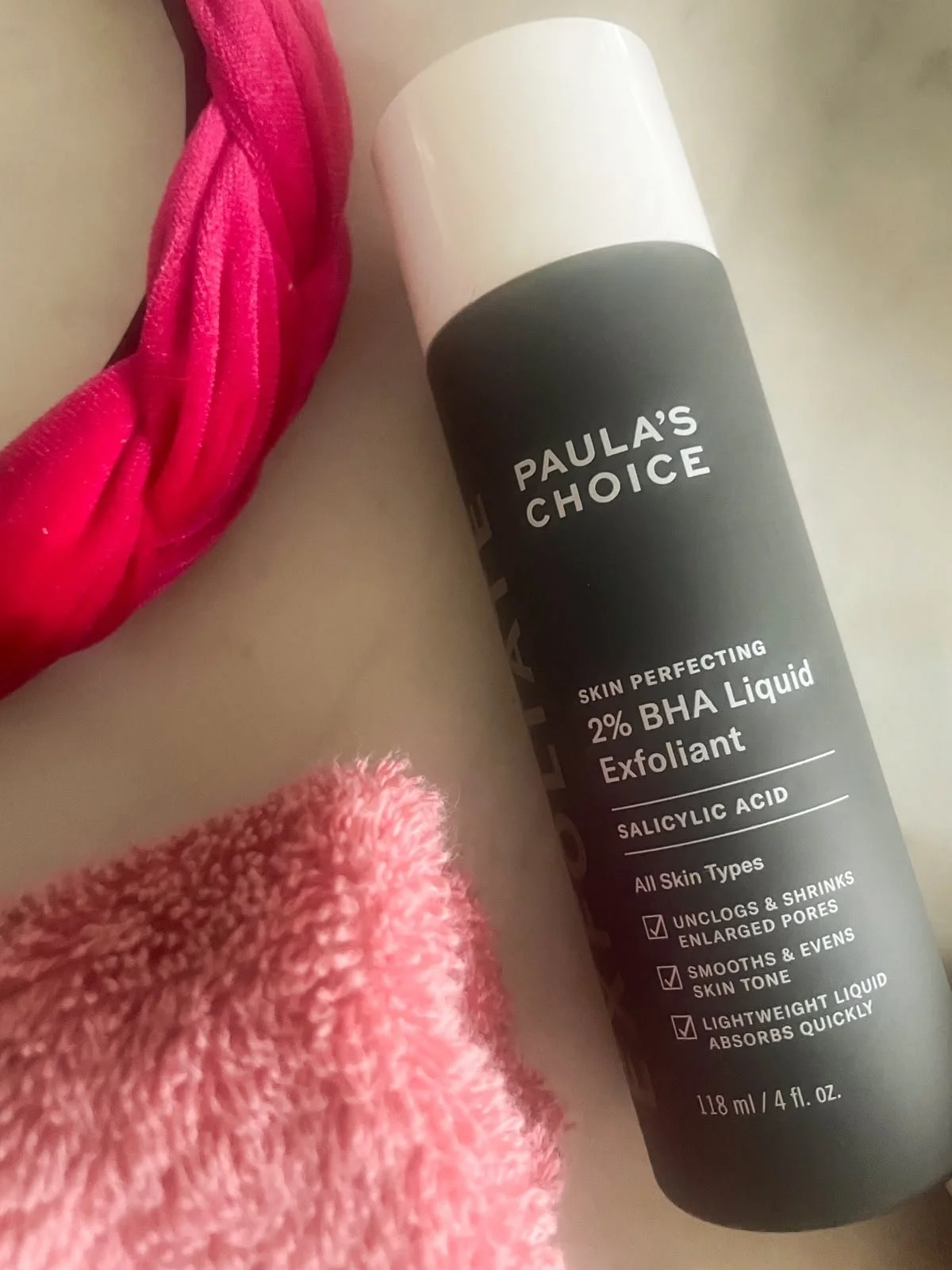 Paula's Choice 2% BHA Liquid Exfoliant on marble with pink towel and headband