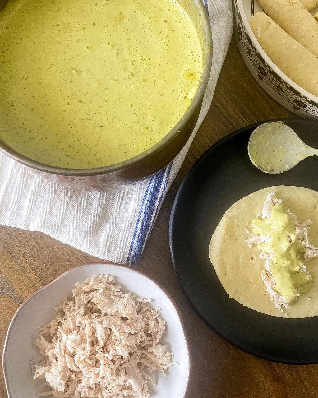 Mise en place for enchiladas suizas — salsa verde in copper pot, shredded chicken, tortilla being filled