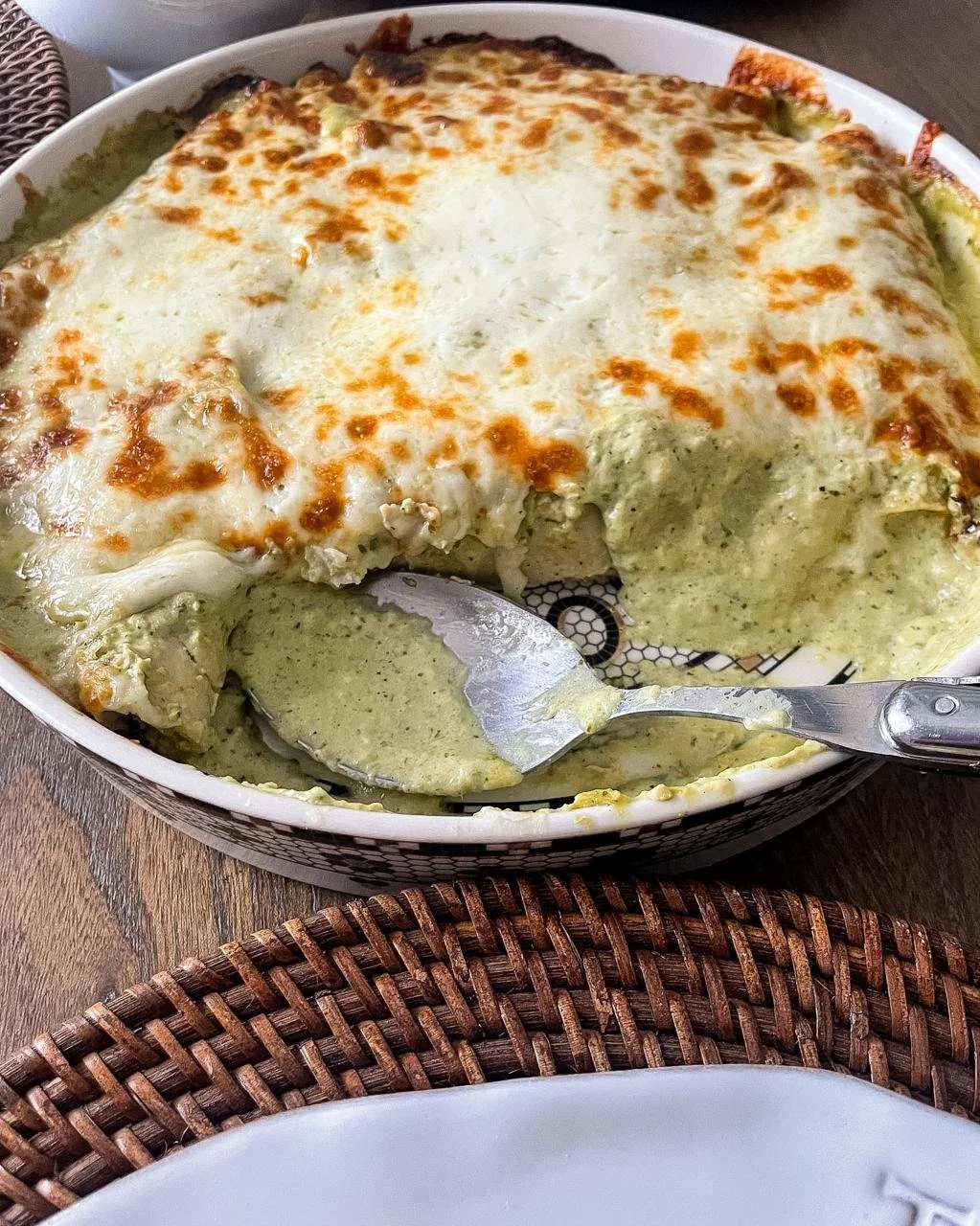 Serving enchiladas suizas from the baking dish, spatula lifting through the creamy salsa verde