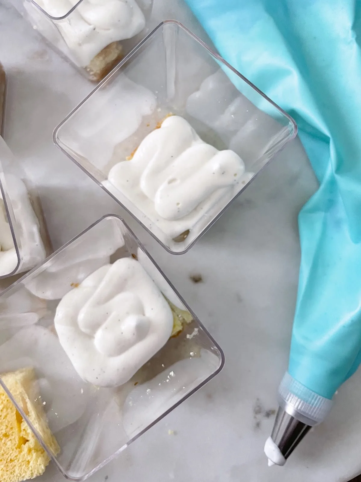Piping cream into individual plastic dessert cups on marble