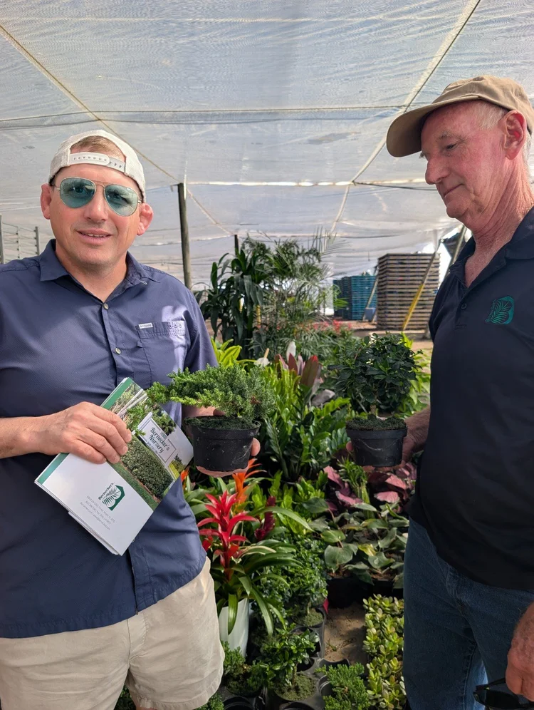 Two growers holding small potted plants beside tropical displays at Bernecker’s