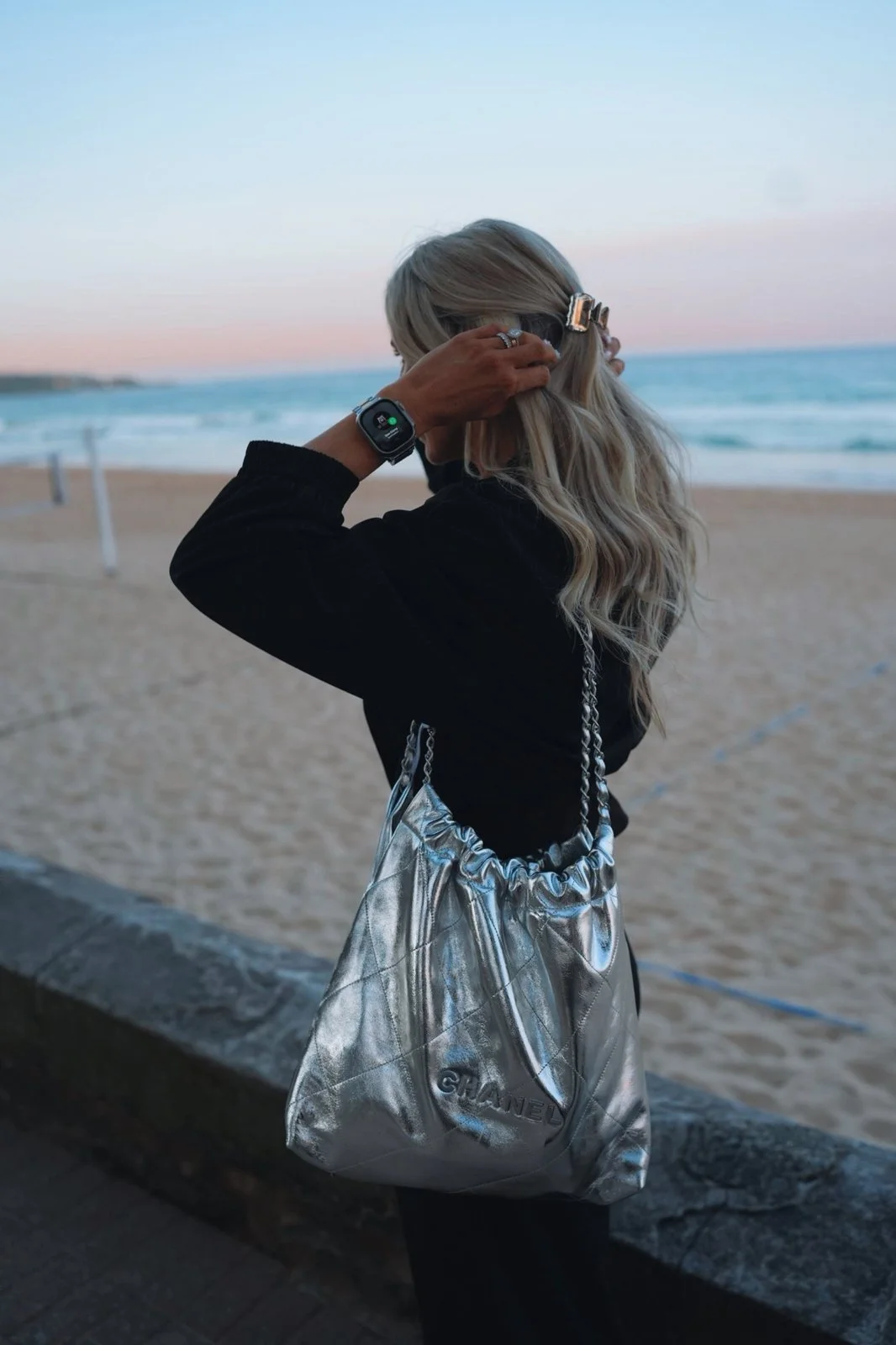 Britt at the beach at sunset with a silver bag