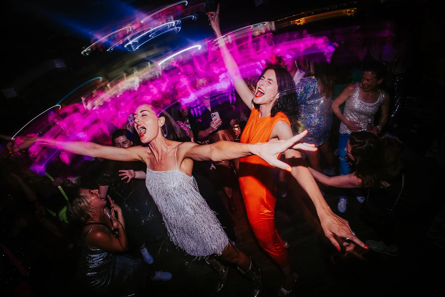 Lise and Sarah dancing with arms flung out under pink lights on the DISCO CLUB floor