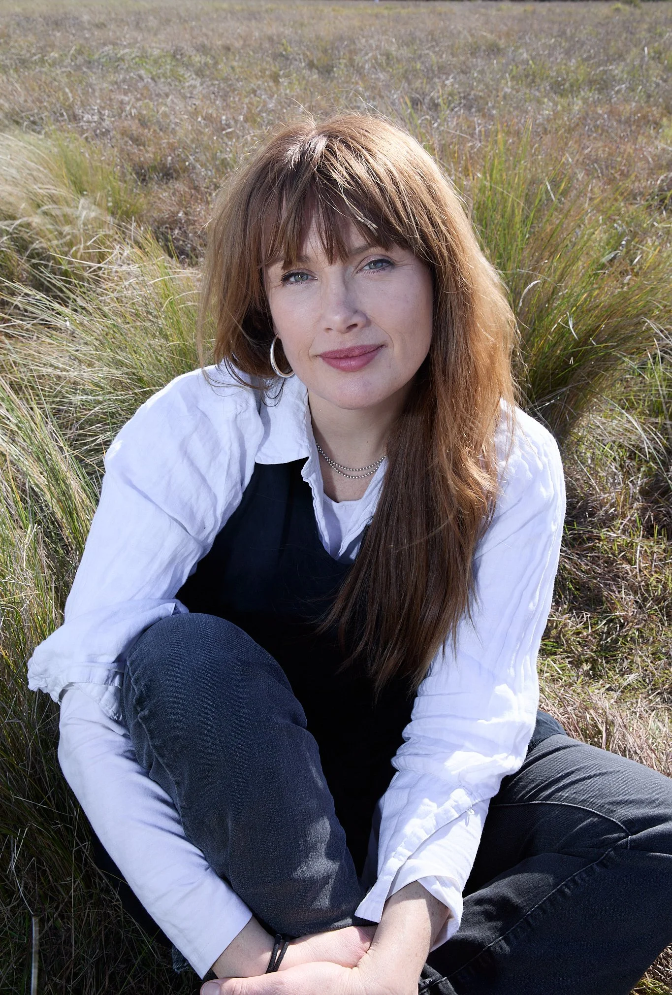 Clare Bowditch outdoors among tall grass, in a white shirt