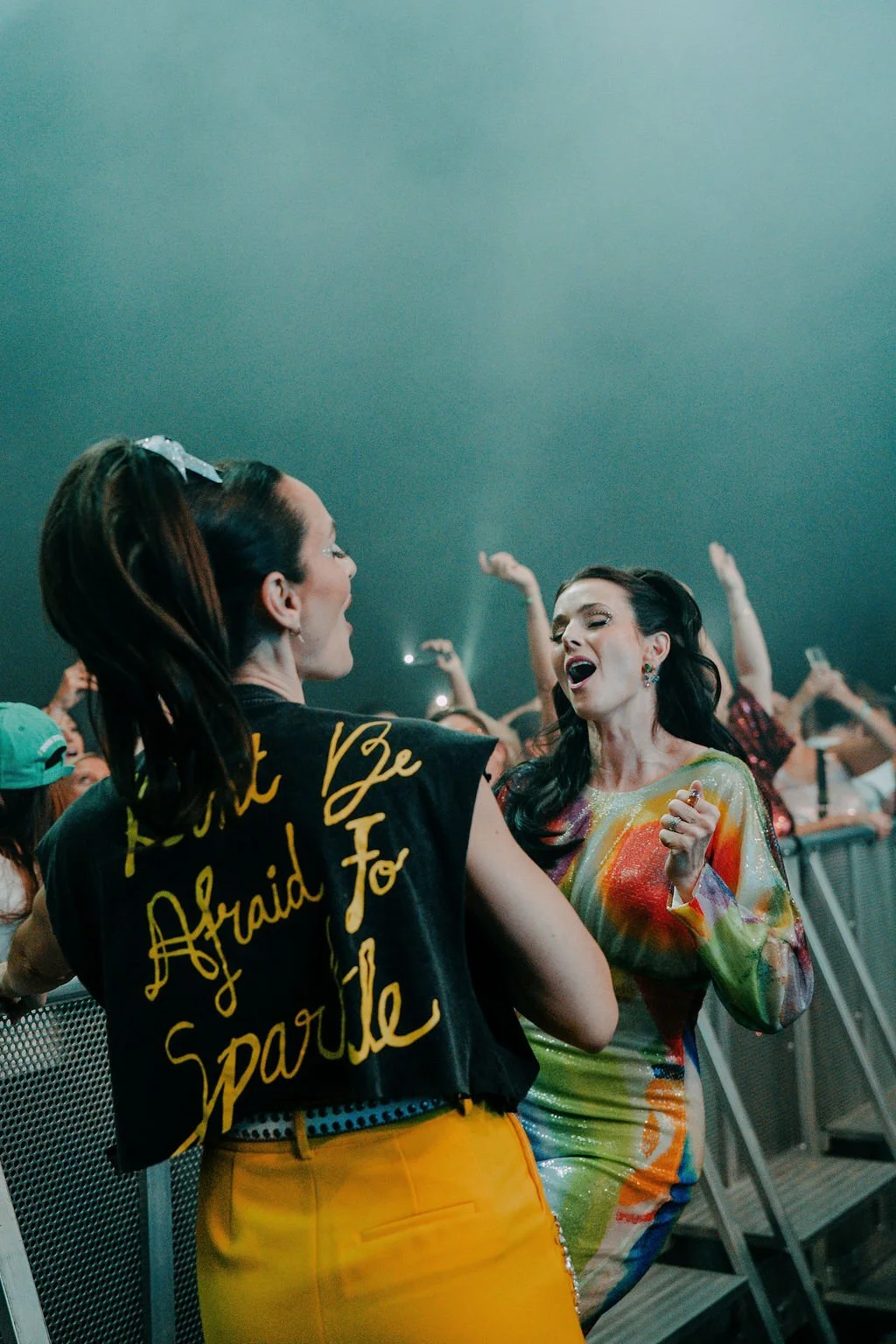 Lise and Sarah singing in the crowd at DISCO CLUB, one wearing a jacket that reads Don't Be Afraid To Sparkle