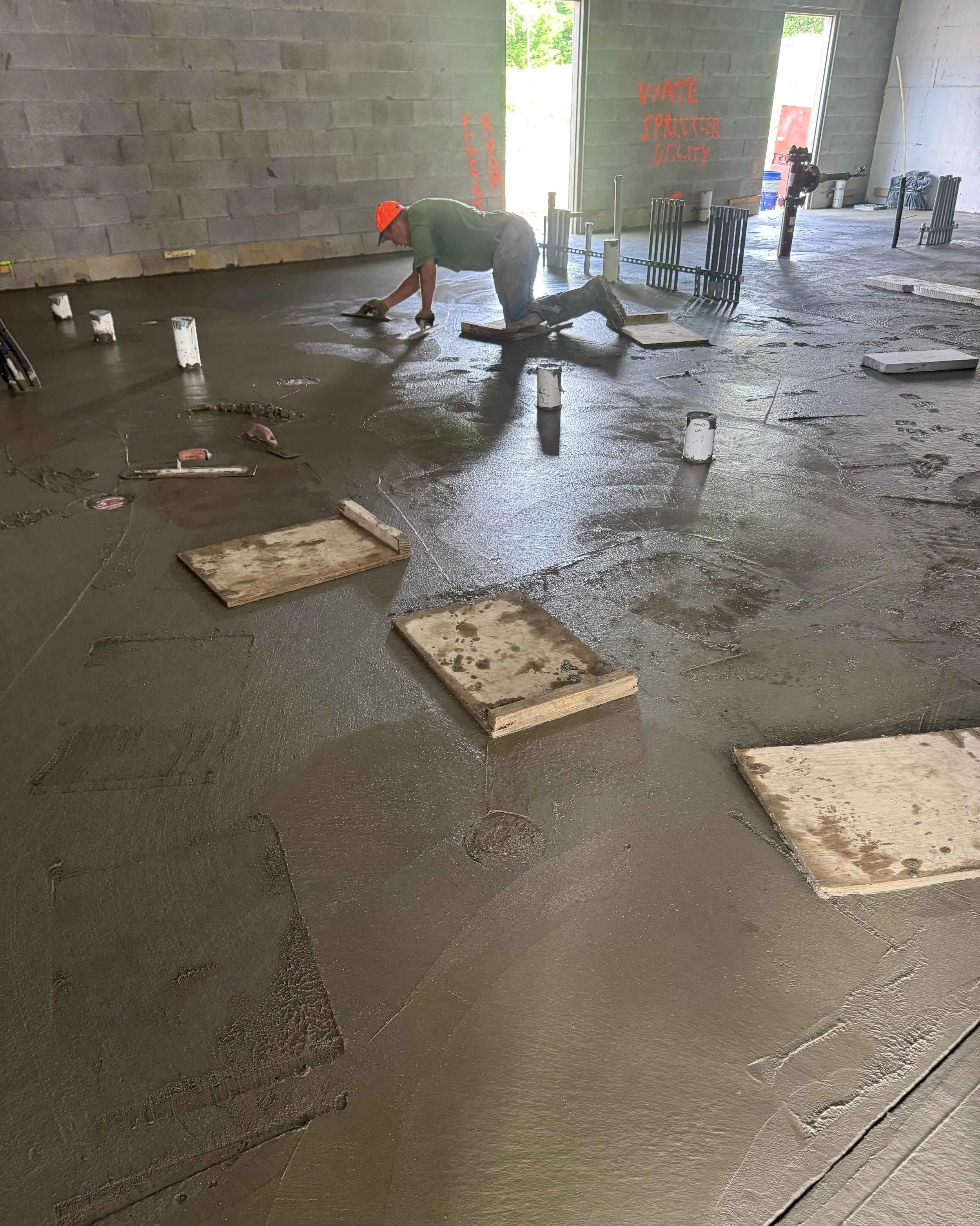 Concrete finisher hand-troweling the dining room slab on kneeboards during construction at Common Ground Kitchen & Taps in McMurray, PA.