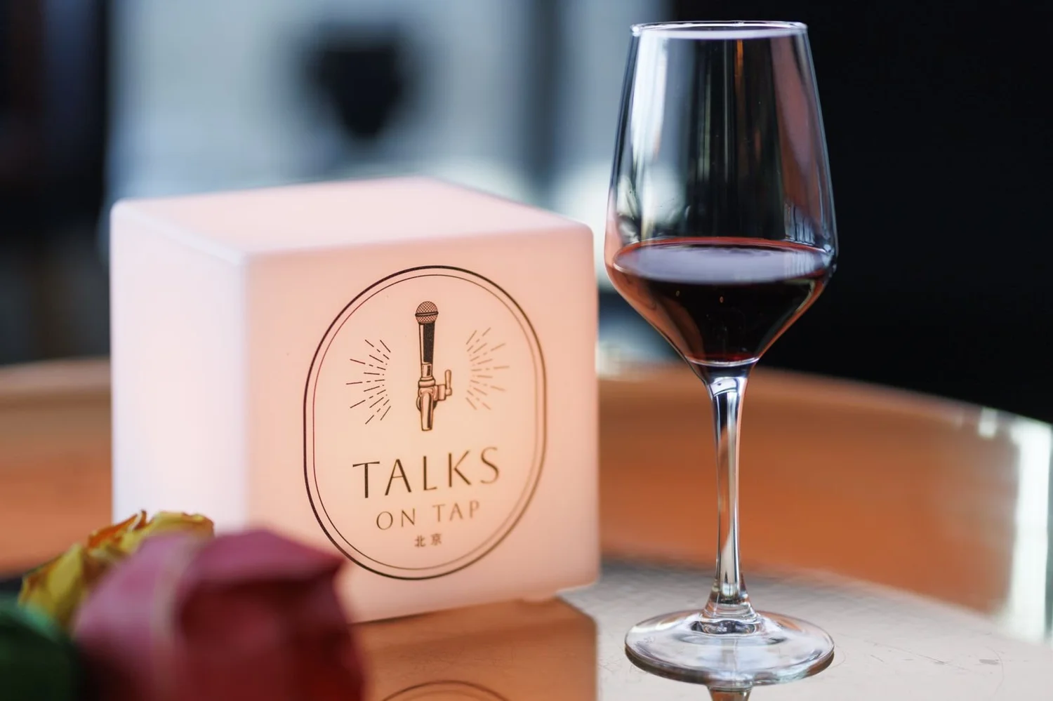 The glowing Talks on Tap Beijing cube beside a glass of red wine