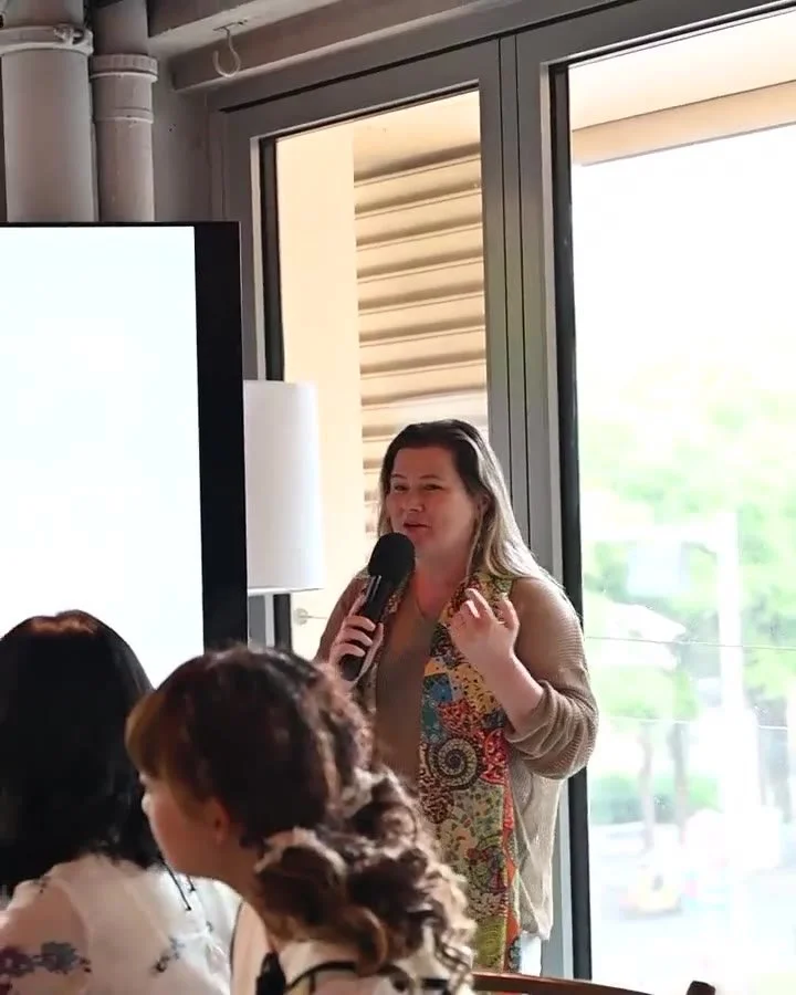 Janice Stewart-Yates speaking with a microphone to guests seated at tables