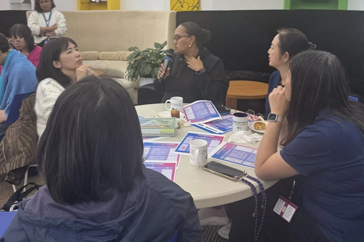 Small group around a table in conversation, worksheets and coffee mugs in front of them