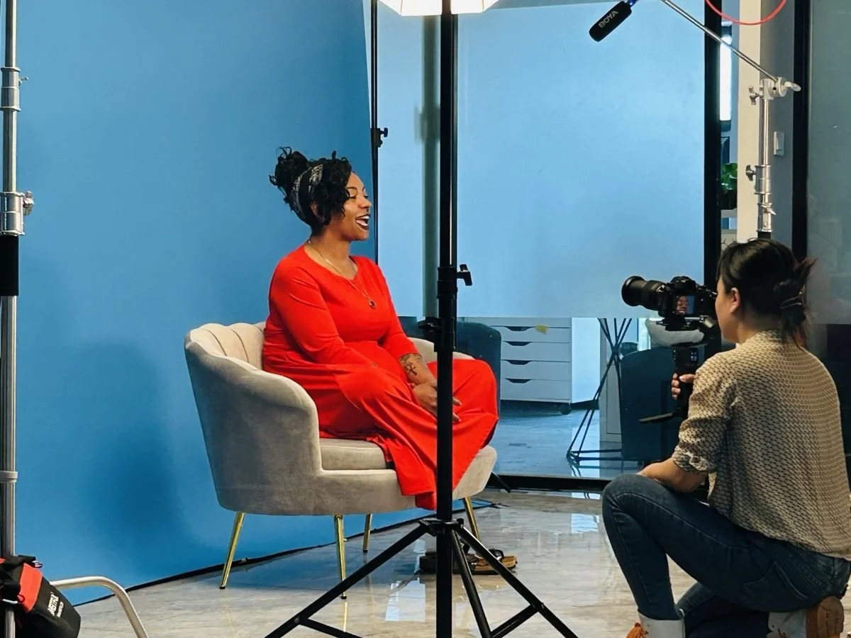 Behind the scenes: an interviewee in red laughing mid-answer as the camera operator films her in front of a blue backdrop