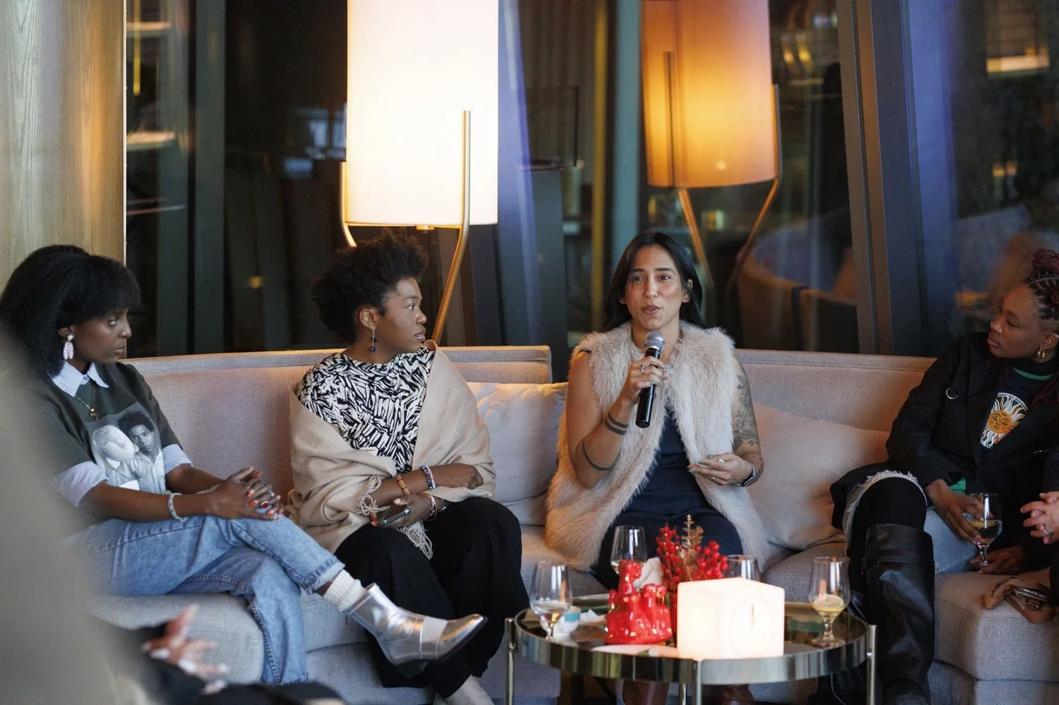Guests on a sofa passing the microphone during a guided dialogue, with the glowing Talks on Tap cube on the table