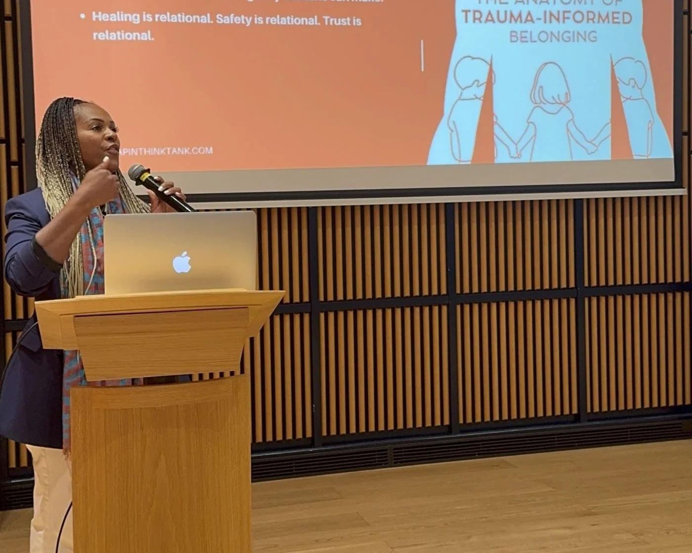 Nicole speaking at a podium in front of a slide on trauma-informed belonging at SENIA Beijing