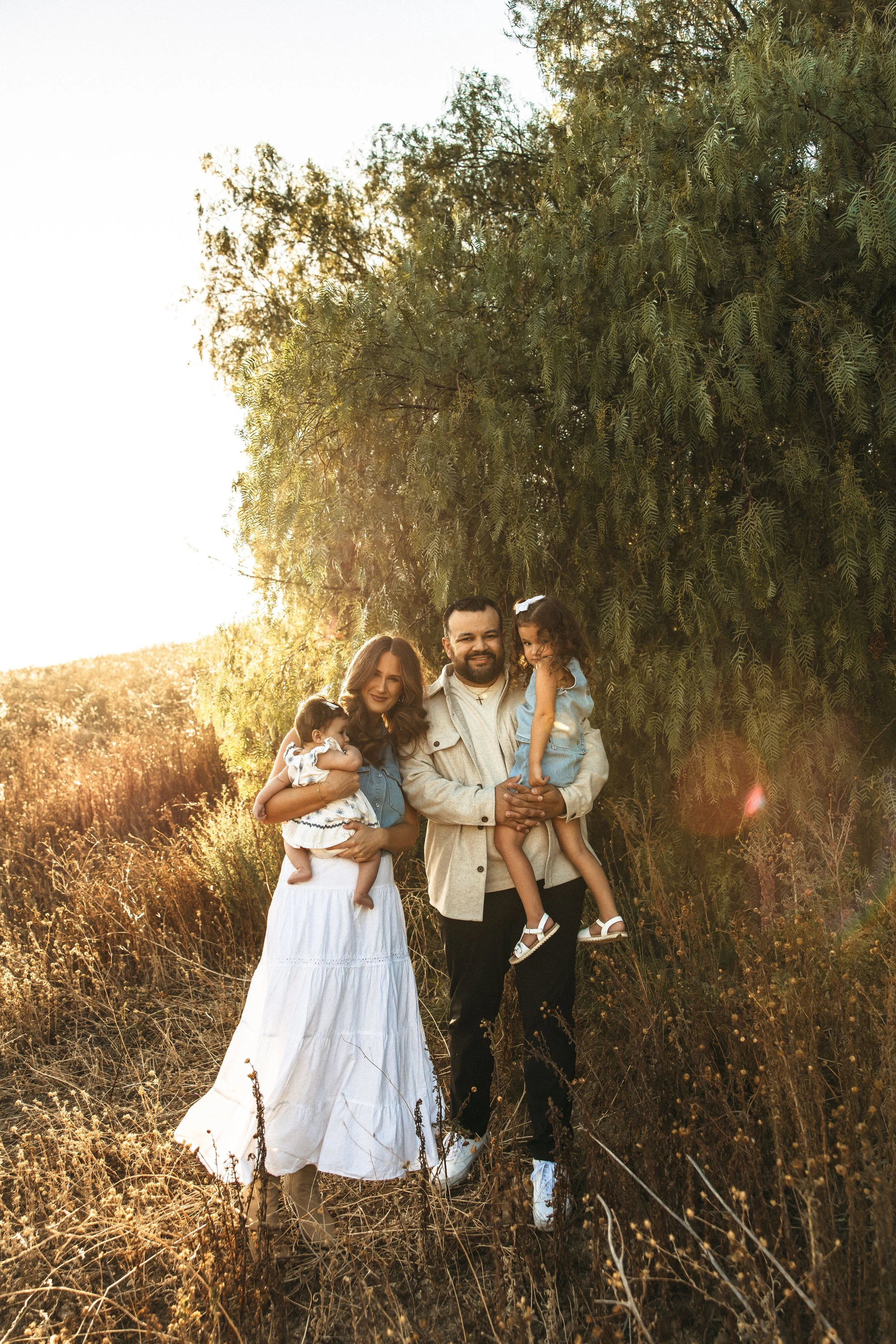 Family maternity portrait of parents sitting with their children in a golden field at sunset.