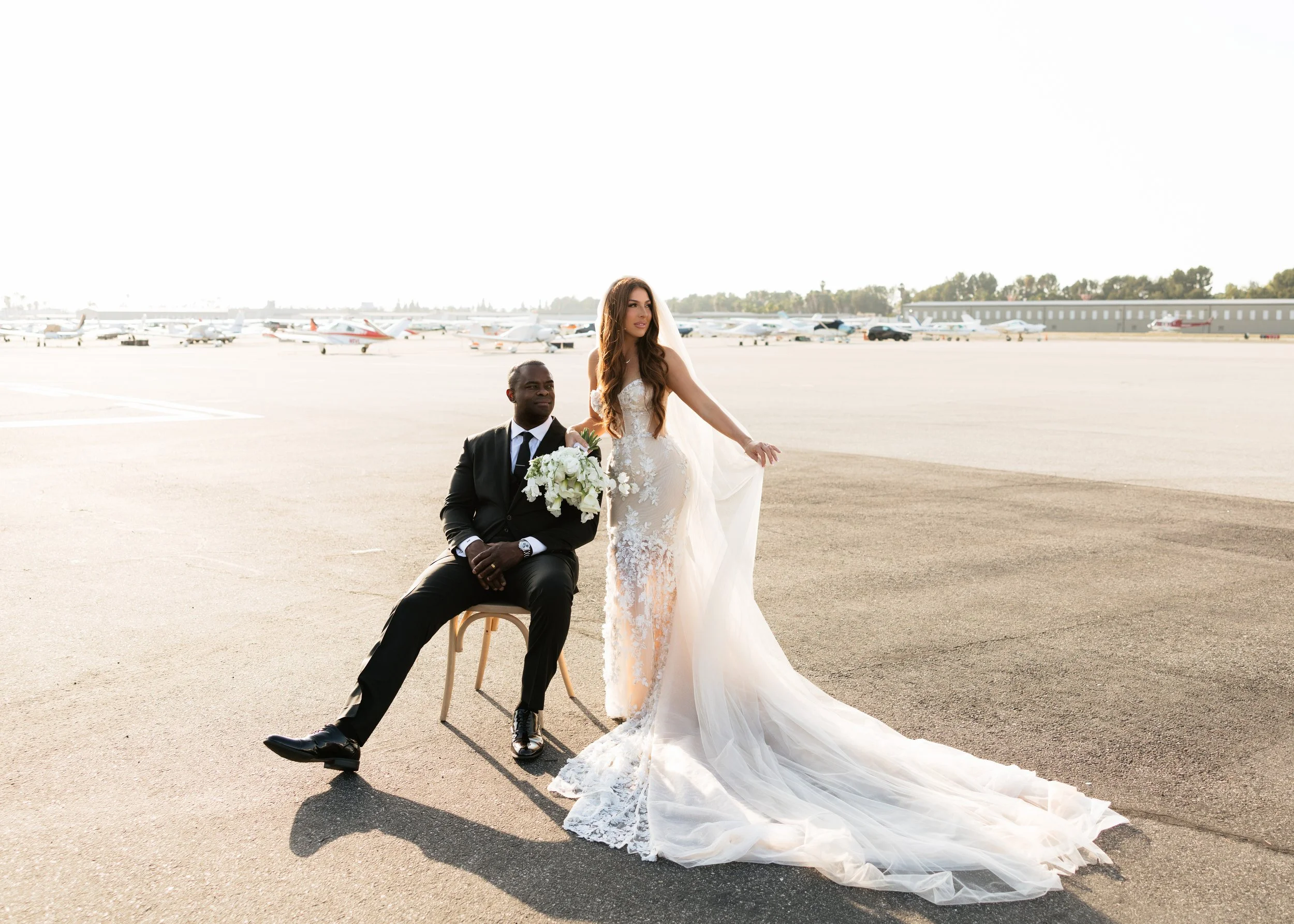 Editorial wedding portrait of a bride and groom on an airport runway with small planes in the background.